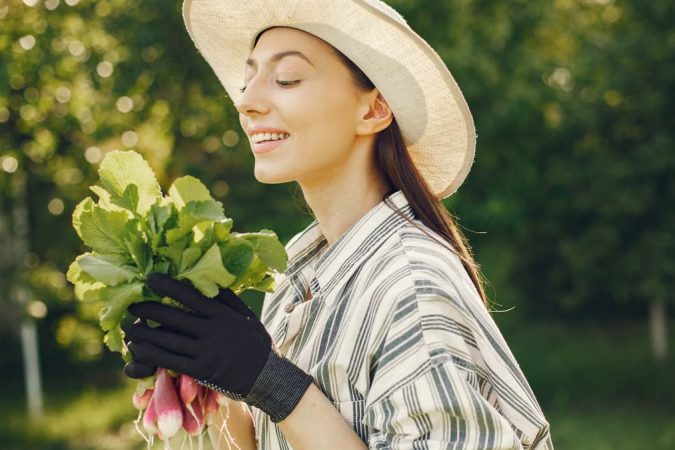 Happy woman enjoying a fresh harvest of radishes in a sunny garden.
